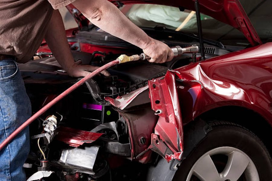 Closeup photo of an auto body mechanic using a compressed air wrench to remove the side fender from a vehicle that was in an auto accident.